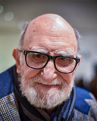 Fotografía del artista en color, calvo y con anteojos